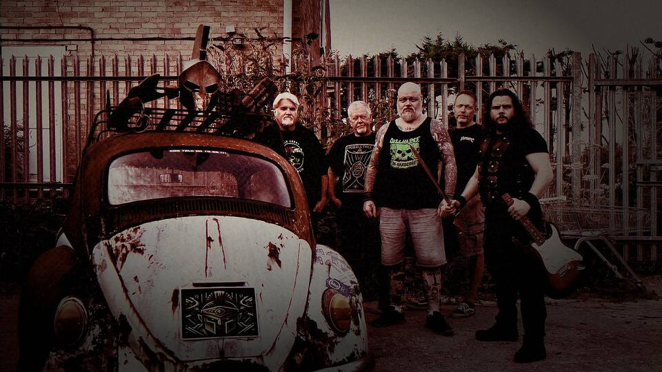 The five members of Kromiius, heavy metal band from Witney, Oxfordshire, standing beside a rusted VW Beetle with a gladiator helmet on its roof rack